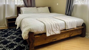 Un lit en bois avec une literie blanche, un tapis à motifs sombres et des rideaux à une fenêtre.