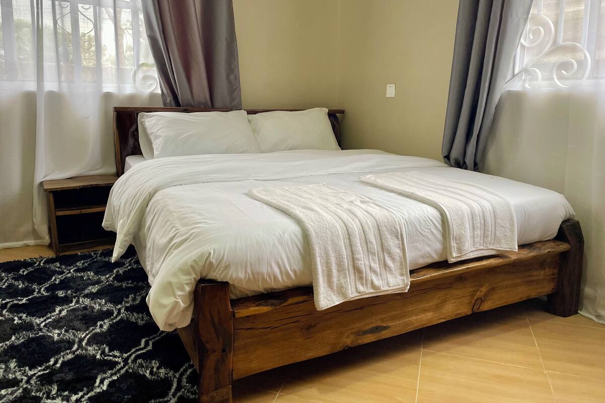 A wooden bed with white bedding, a dark patterned rug, and curtains on a window.