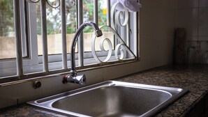 Une cuisine dotée d’un évier en acier inoxydable, d’une fenêtre avec des barreaux en métal et d’un plan de travail en granit.