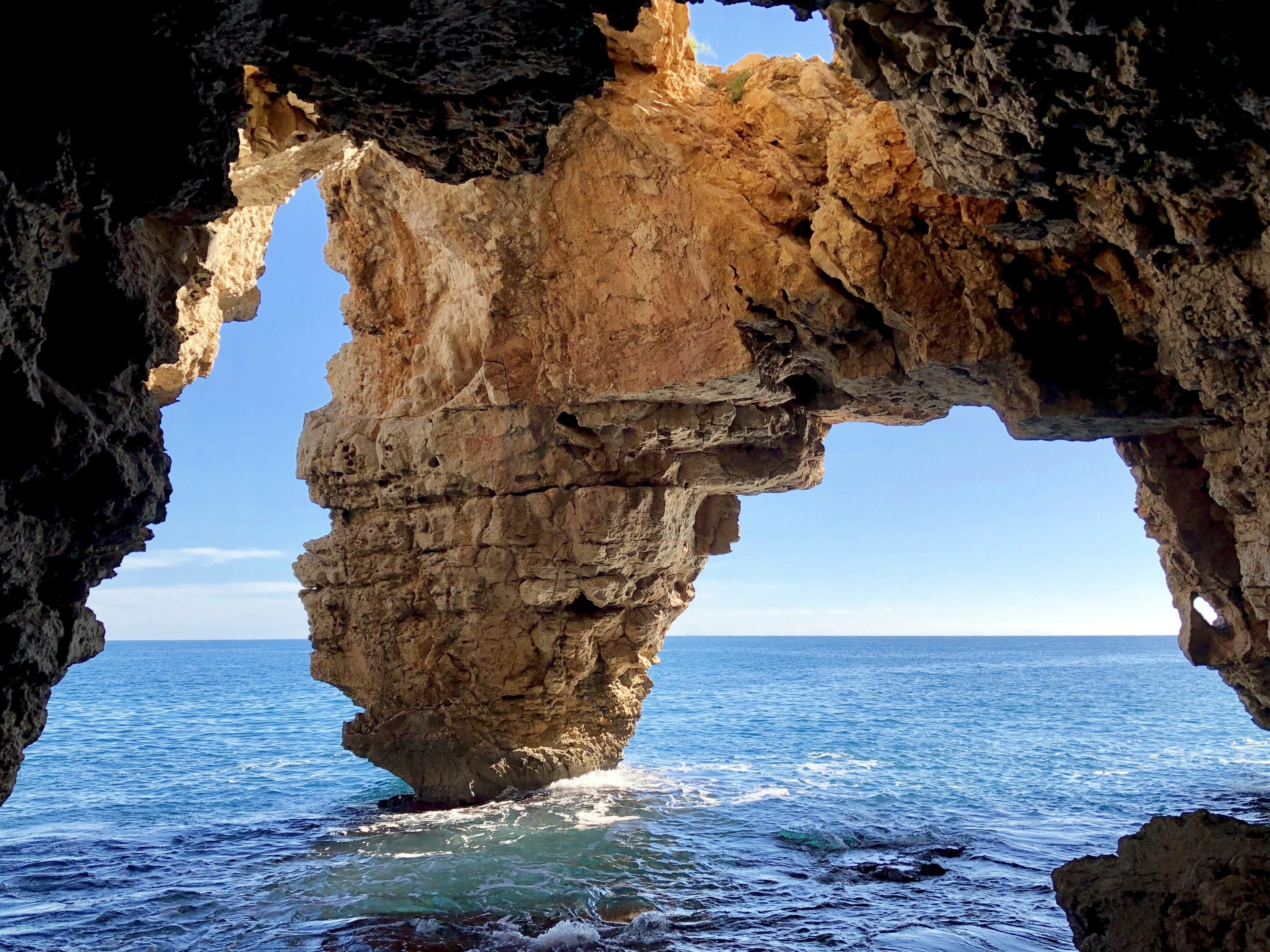 A natural rock formation with a cave-like opening, leading to a view of the ocean.