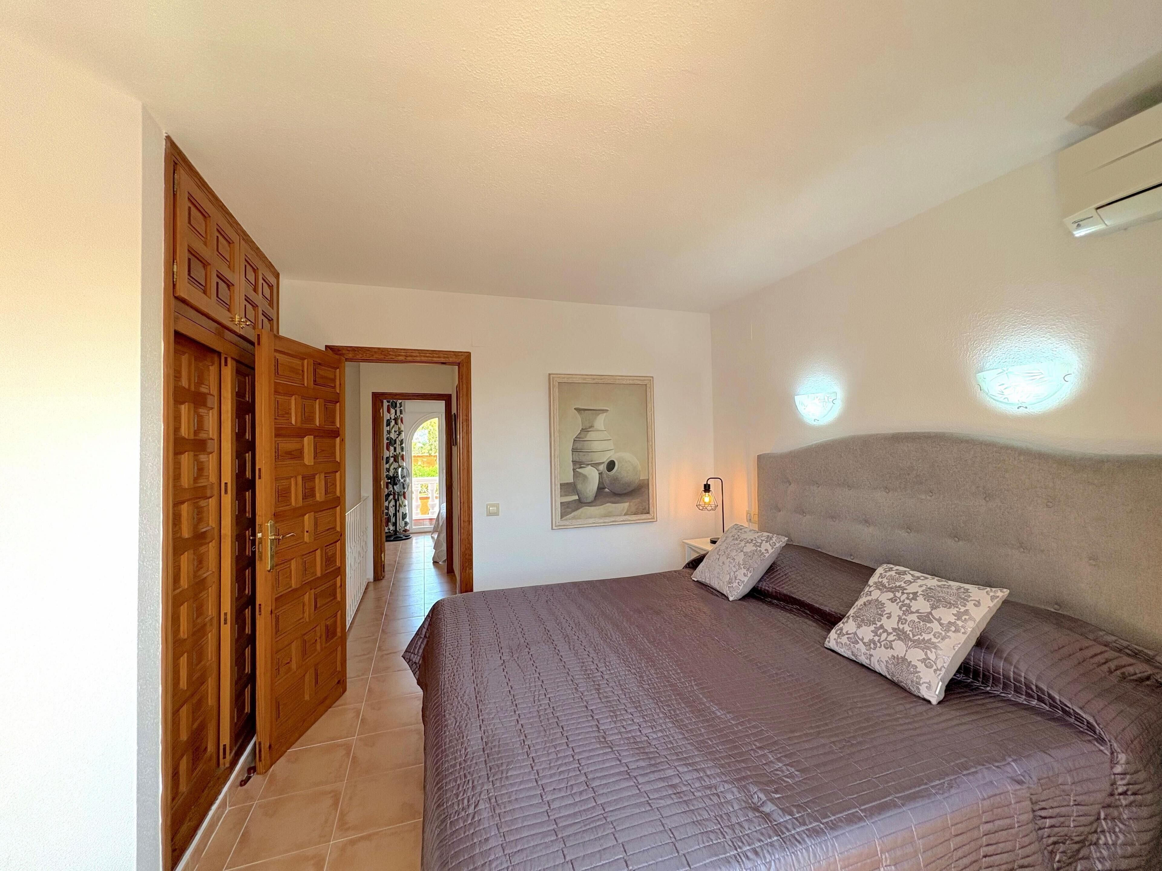 Quarto com cama grande, armário de madeira e corredor que dá para área externa.