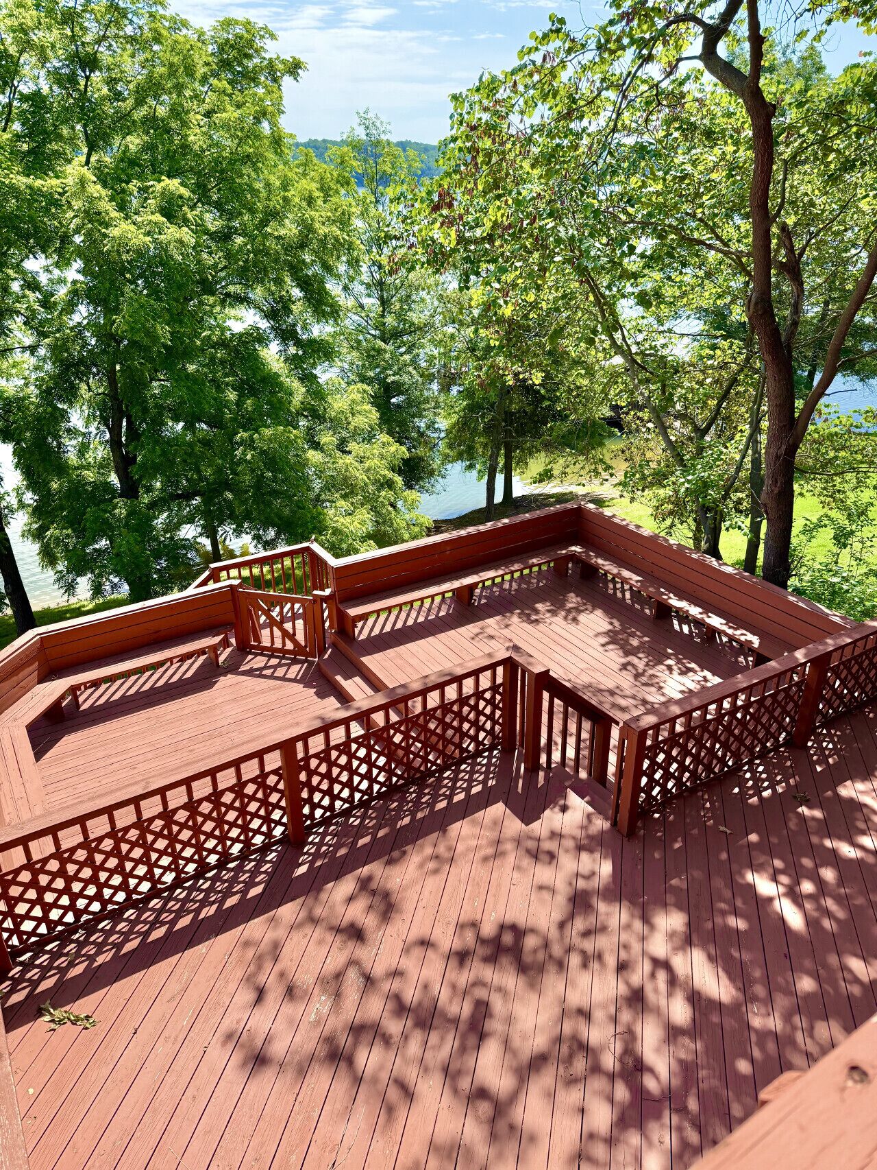 A wooden deck with a red railing, overlooking a lake surrounded by trees.