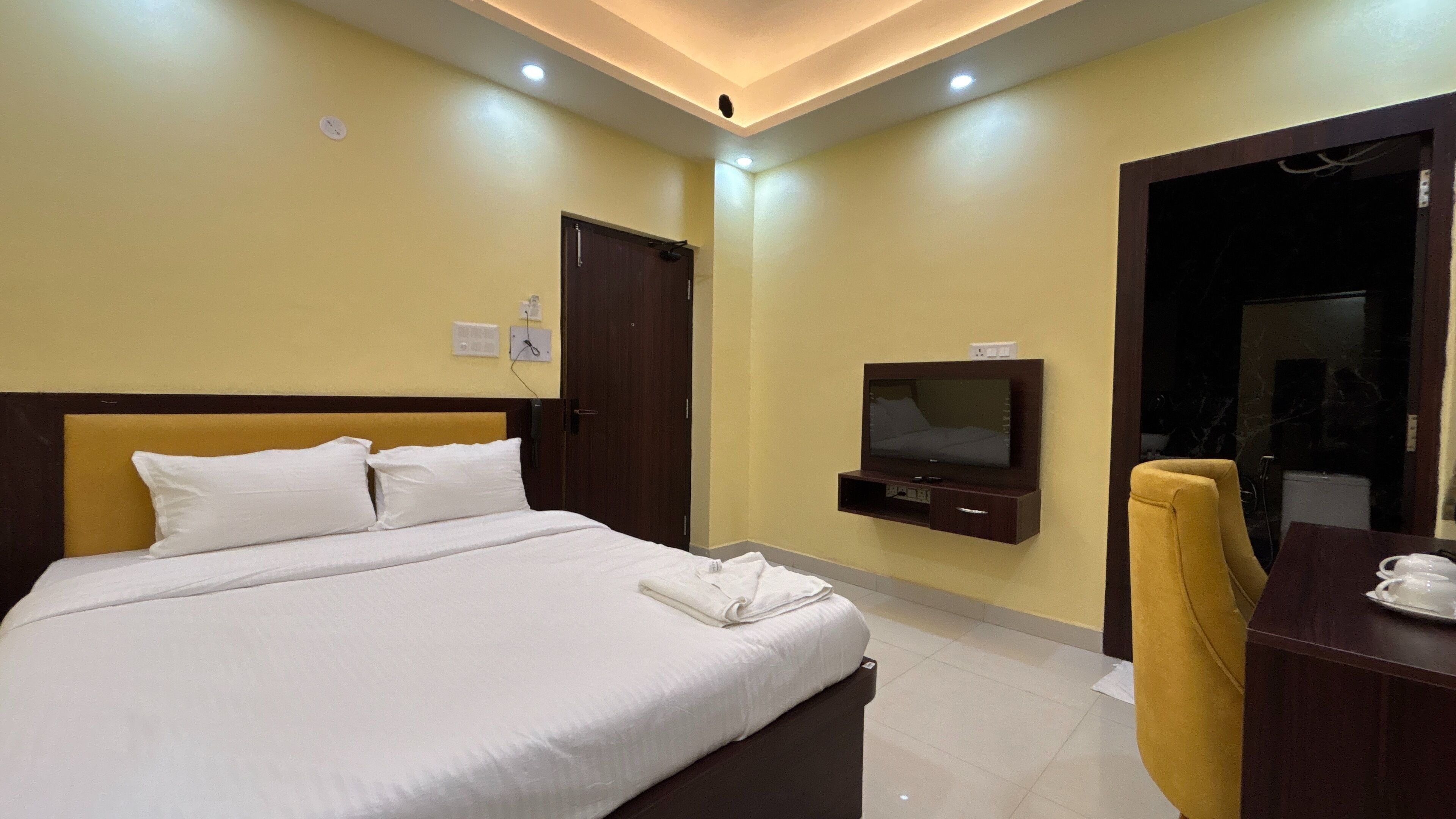 Una habitación de hotel con una cama, un televisor montado en la pared y un escritorio con una silla.