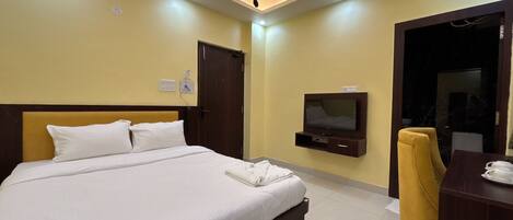 Una habitación de hotel con una cama, un televisor montado en la pared y un escritorio con una silla.