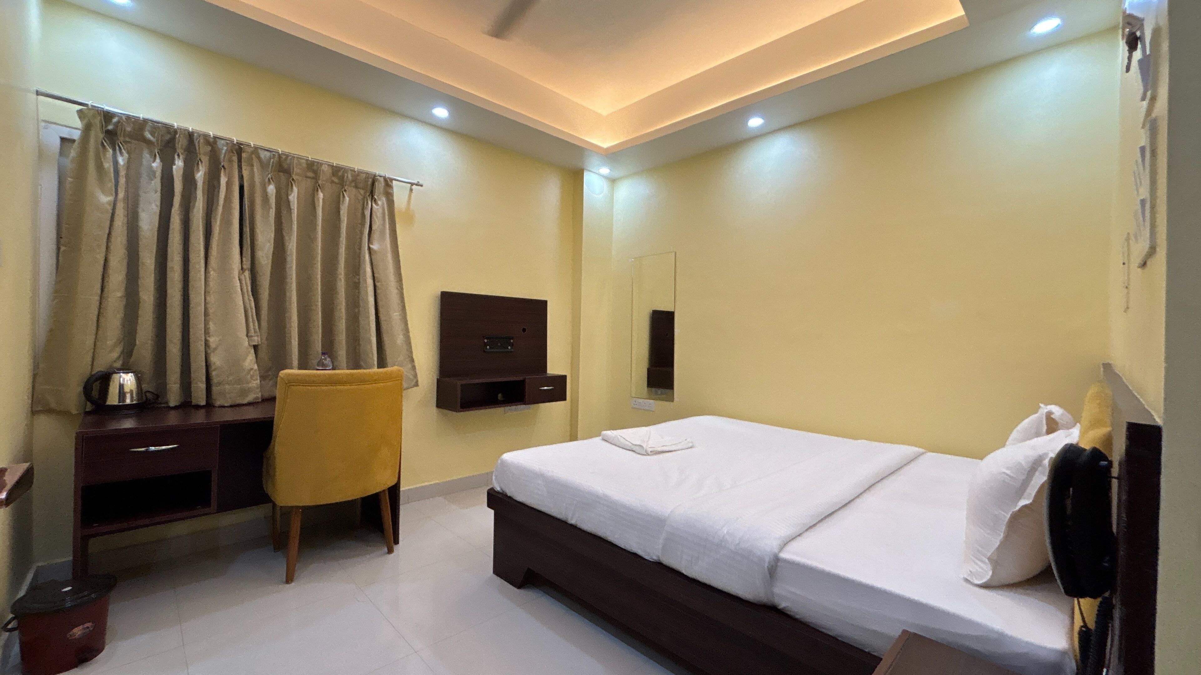 Habitación de hotel con cama, escritorio, silla, espejo y un mueble pequeño.