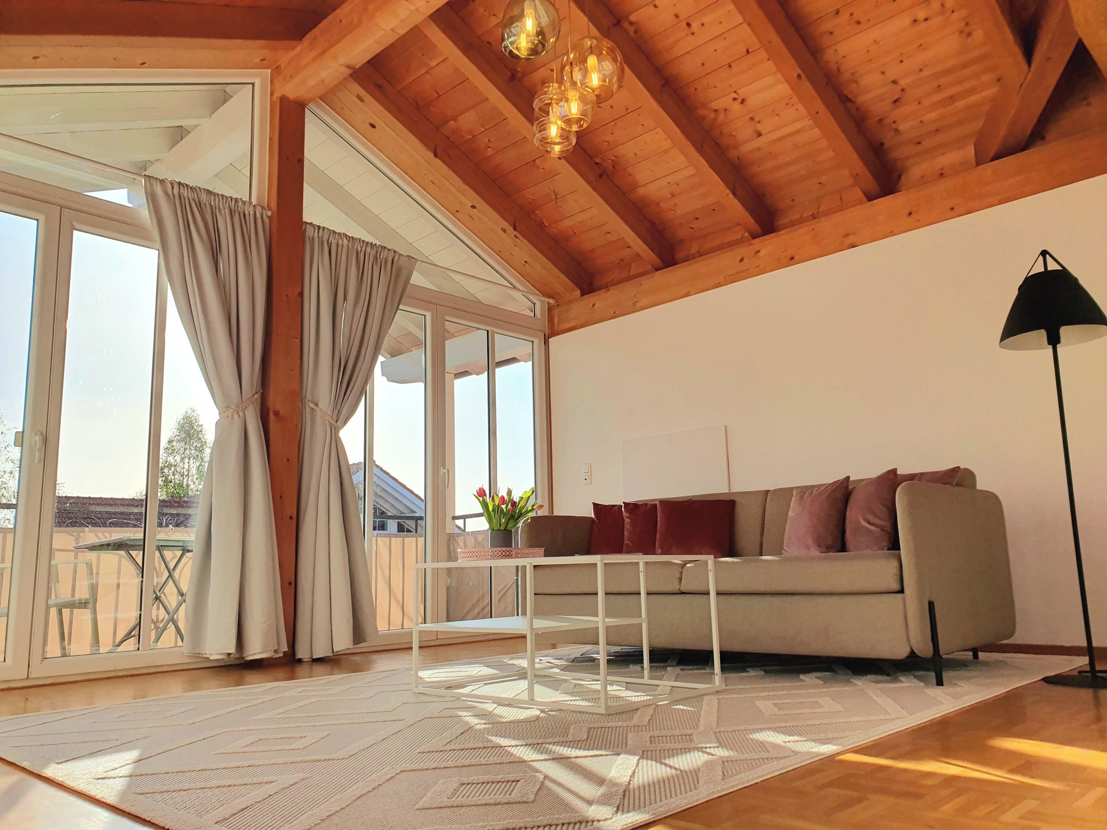 A spacious living room with a wooden ceiling, a sofa, a coffee table, and a floor lamp.