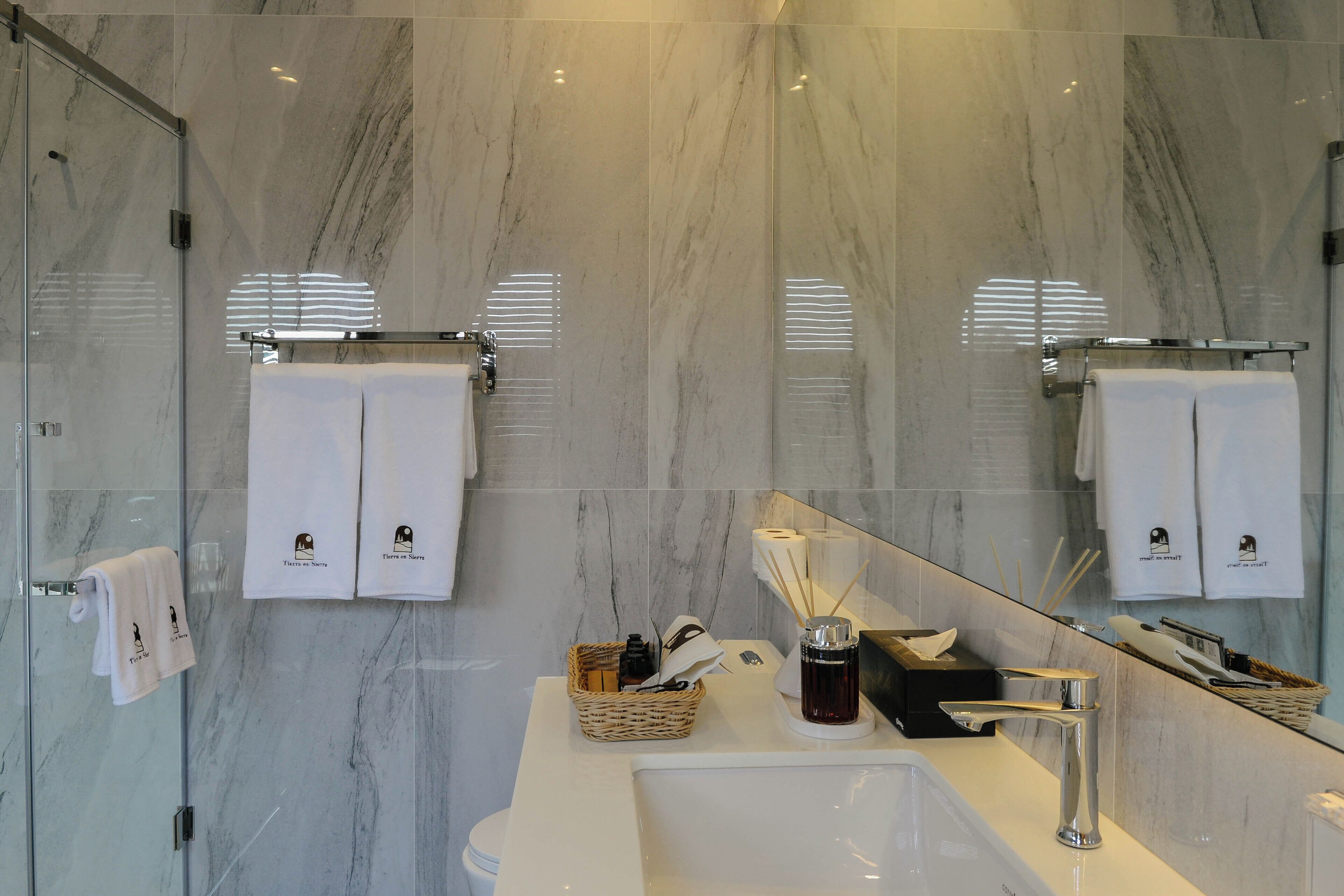A modern bathroom with a marble floor, a glass shower enclosure, a white sink with a chrome faucet, and a mirror reflecting the room.