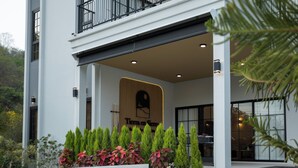 A modern two-story building with a balcony, a wooden sign with text, and a well-maintained garden with various plants. - Tierra en Sierra (Pak Chong)
