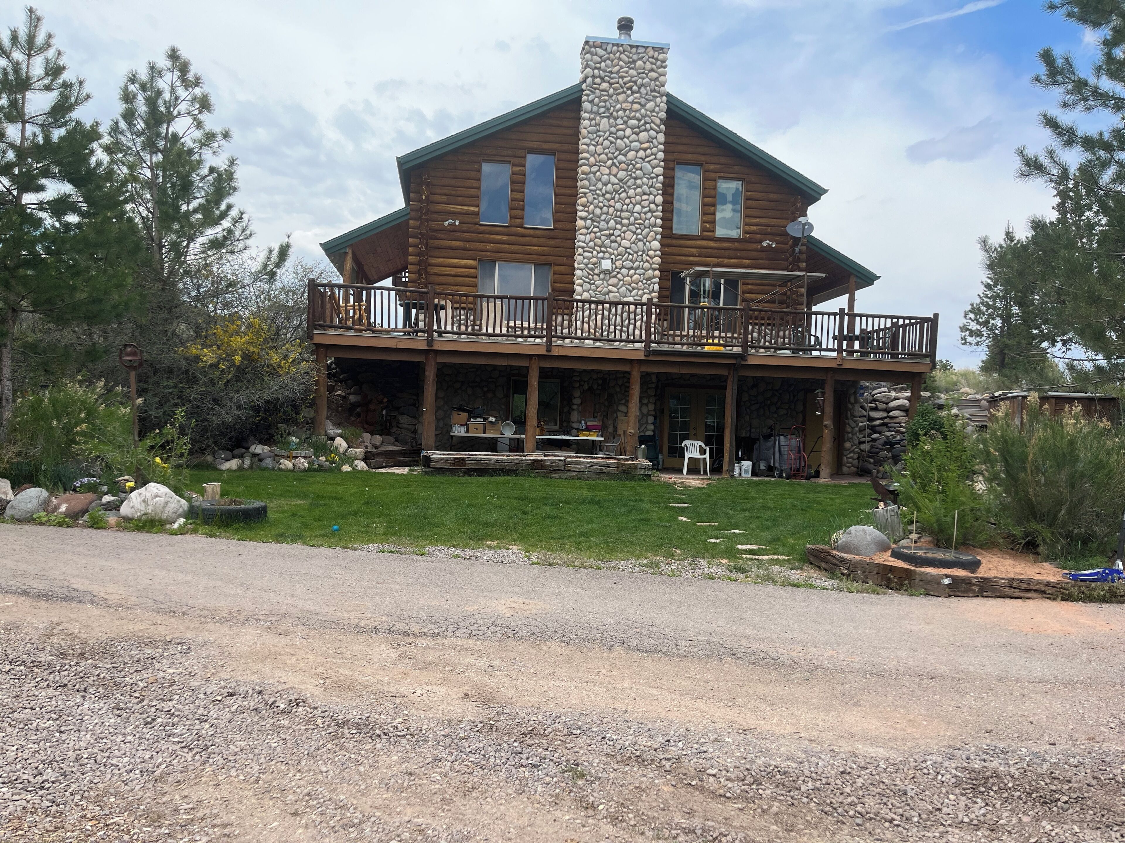 A two-story log cabin with a stone chimney, a covered porch, and a stone wall.