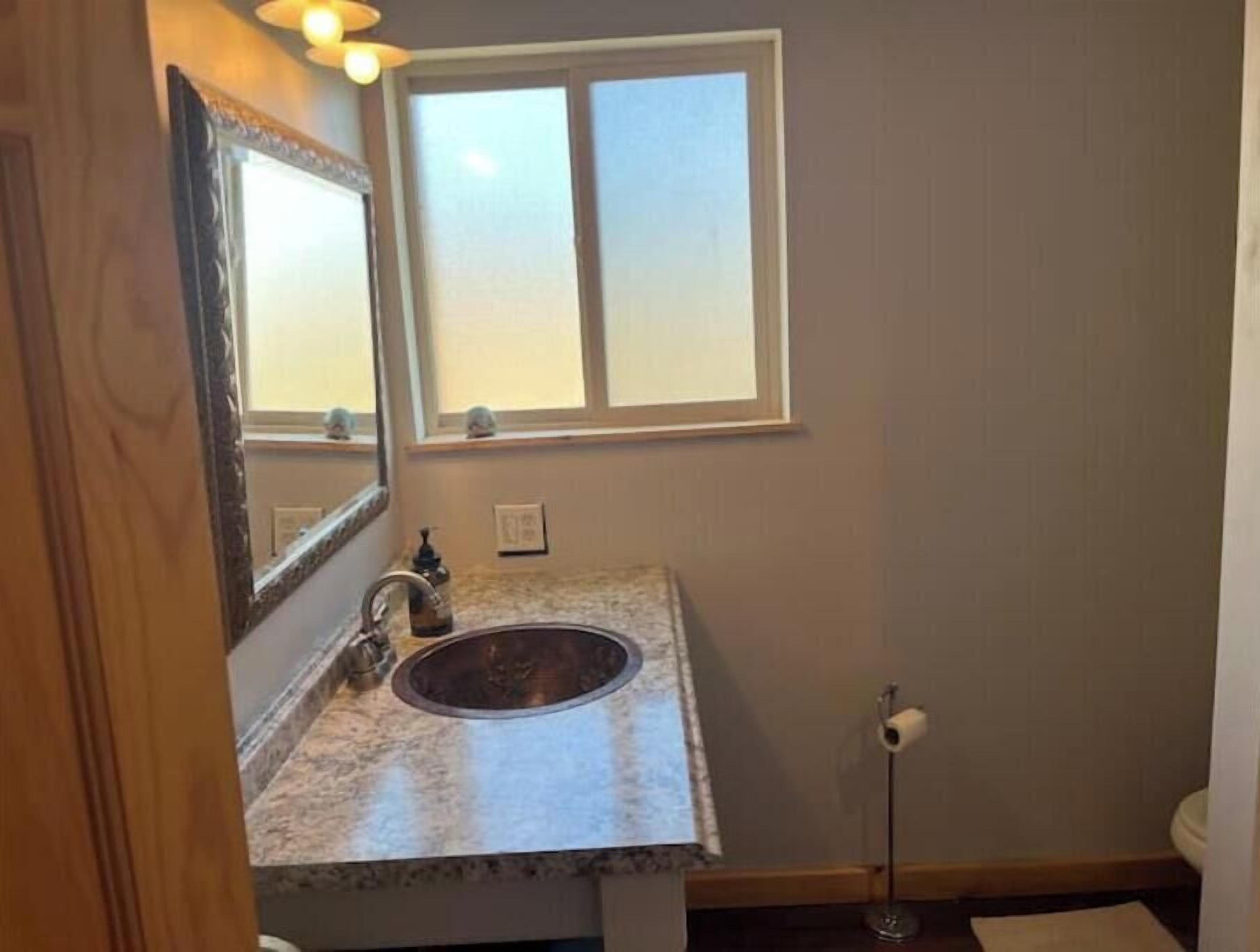A bathroom with a marble sink, a mirror, a window, and a toilet.