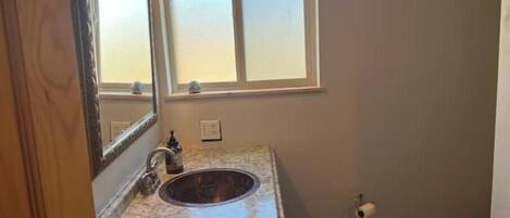 A bathroom with a marble sink, a mirror, a window, and a toilet.