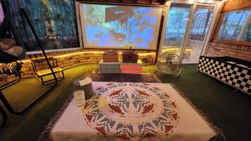 A cozy room with a projector screen displaying 'Coffee Music', a patterned rug, and a checkered bench.