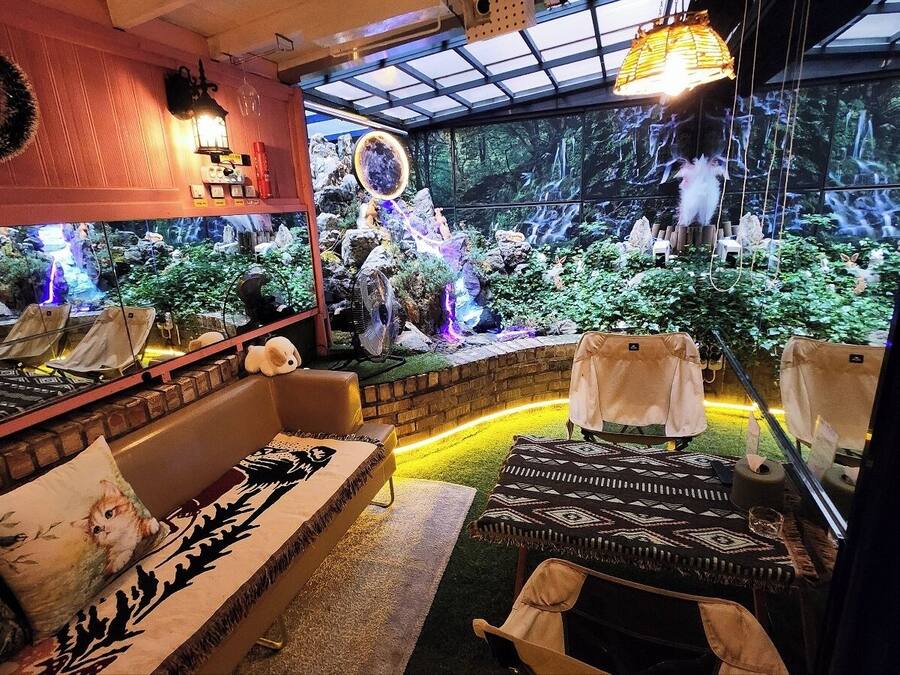 A cozy indoor seating area with a large aquarium, comfortable sofas, and a view of a waterfall through a glass wall.