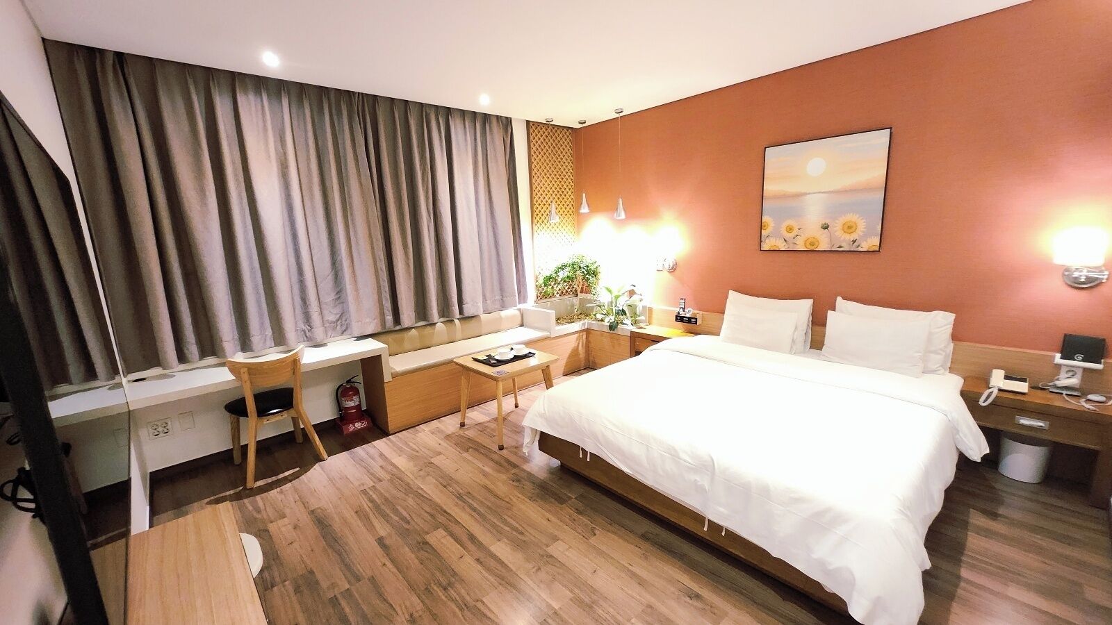 A hotel room with a bed, desk, chair, and a small table with a plant.