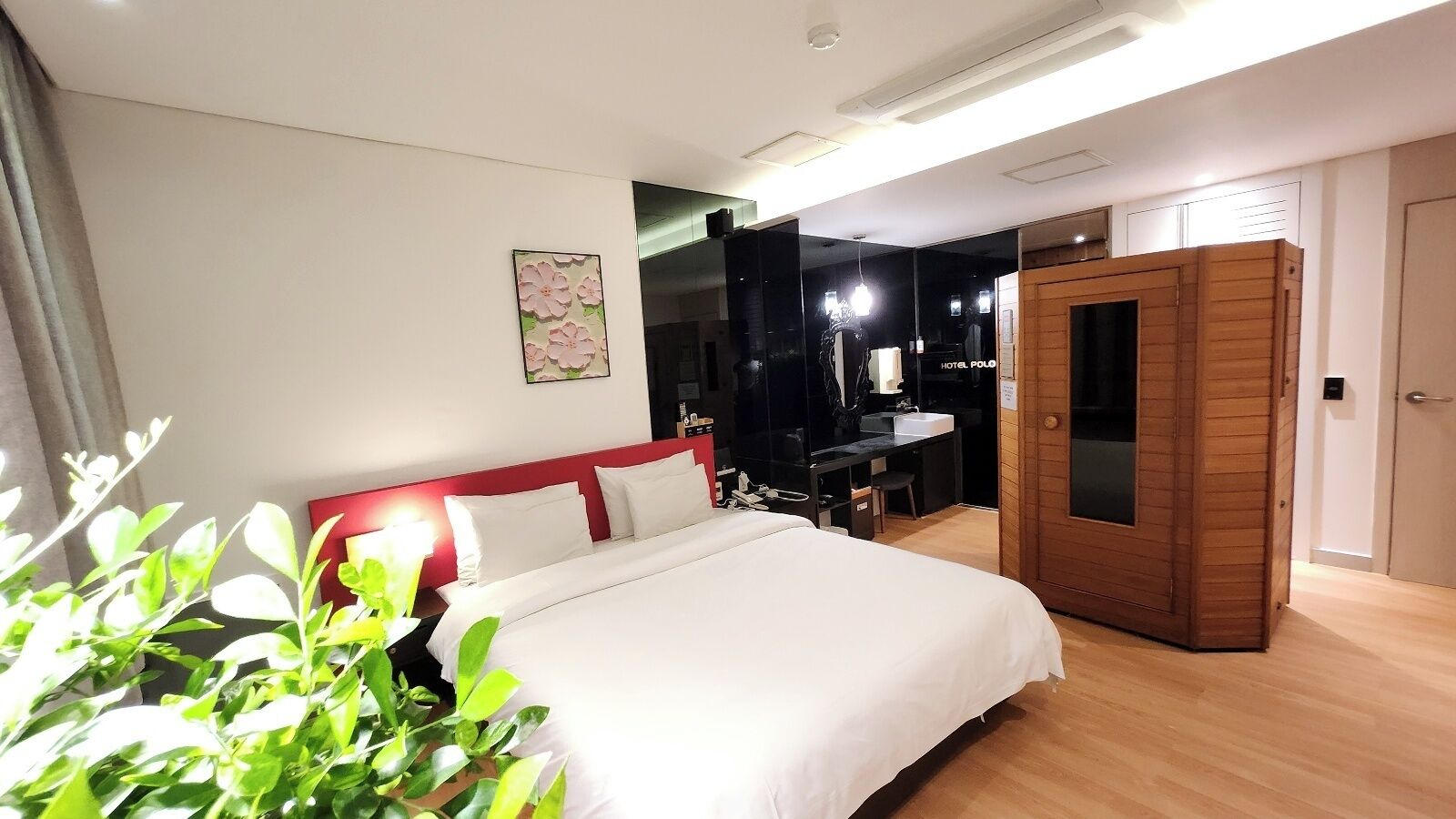 A hotel room with a bed, a desk, a mirror, and a wooden wardrobe.