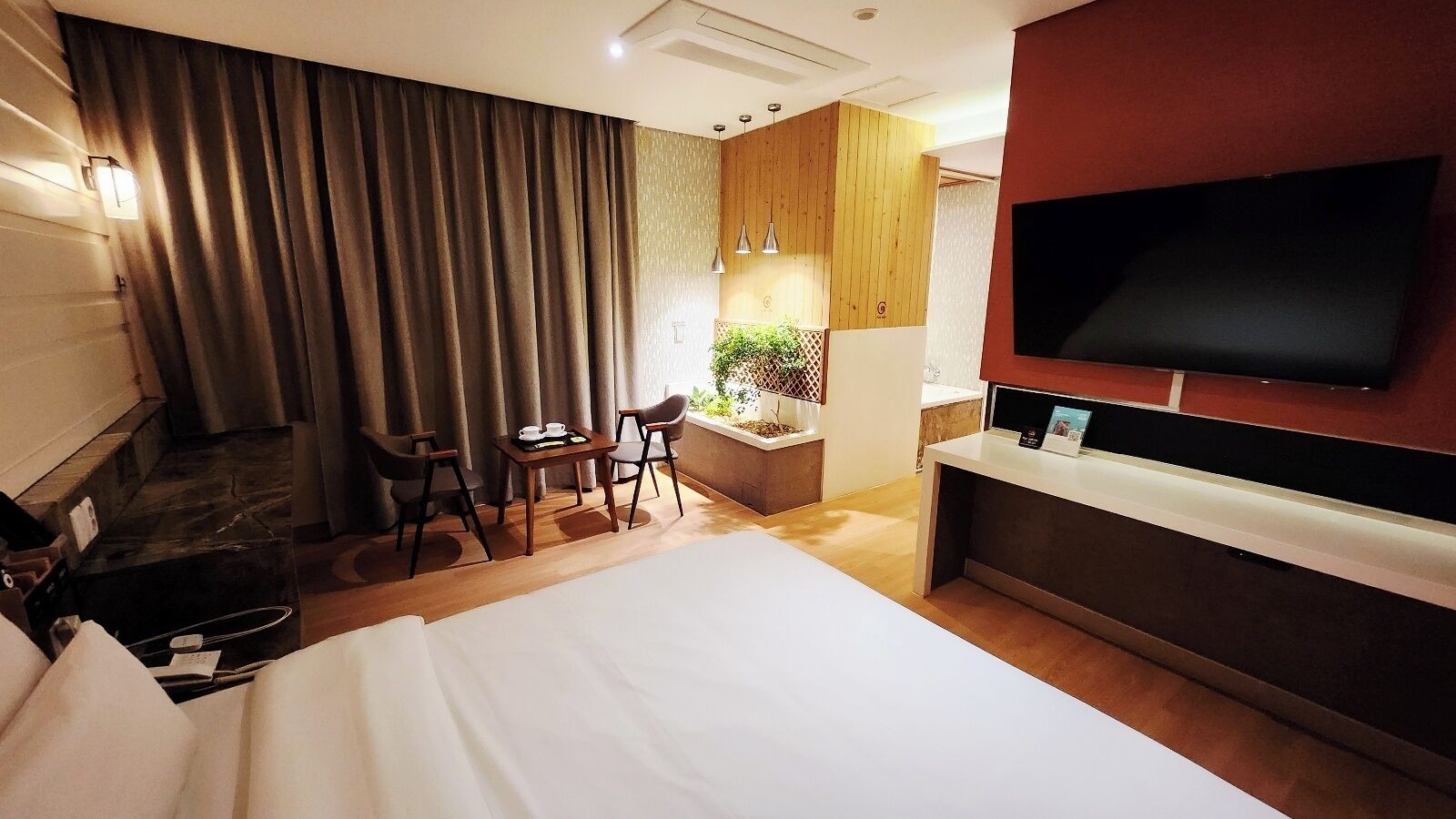 A hotel room with a large bed, a desk with a chair, a TV mounted on the wall, and a window with curtains.