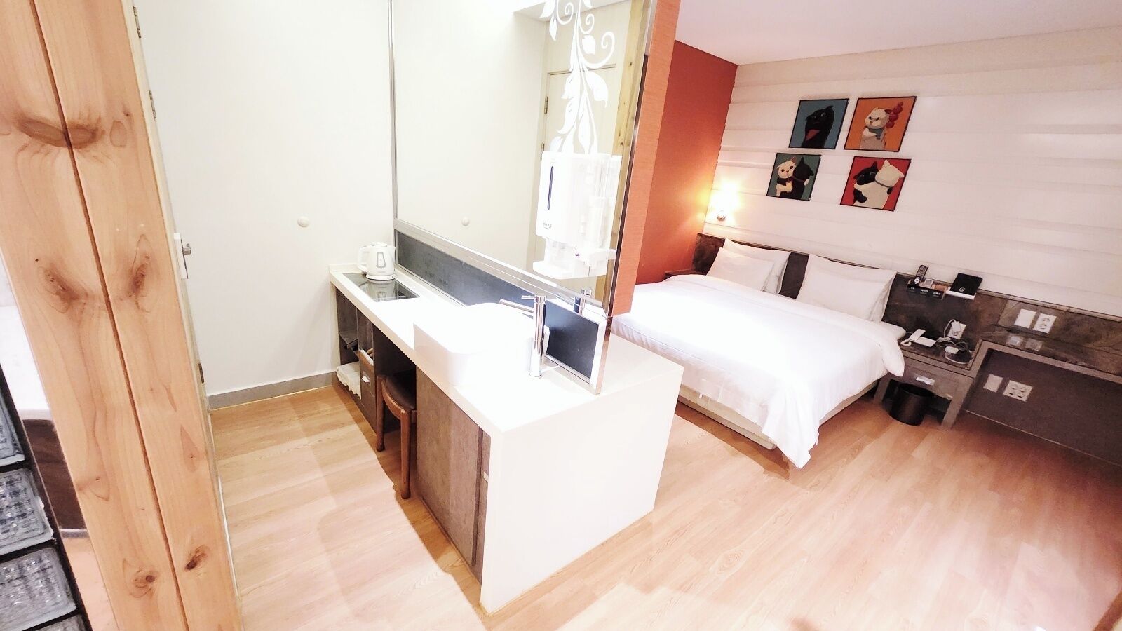 A compact hotel room with a bed, a small desk, a mirror, and a bedside table.