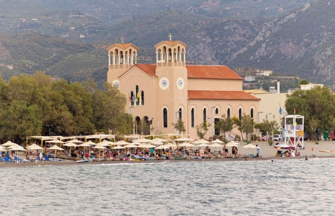 Une église côtière dotée d’un clocher, entourée de parasols de plage et de personnes.