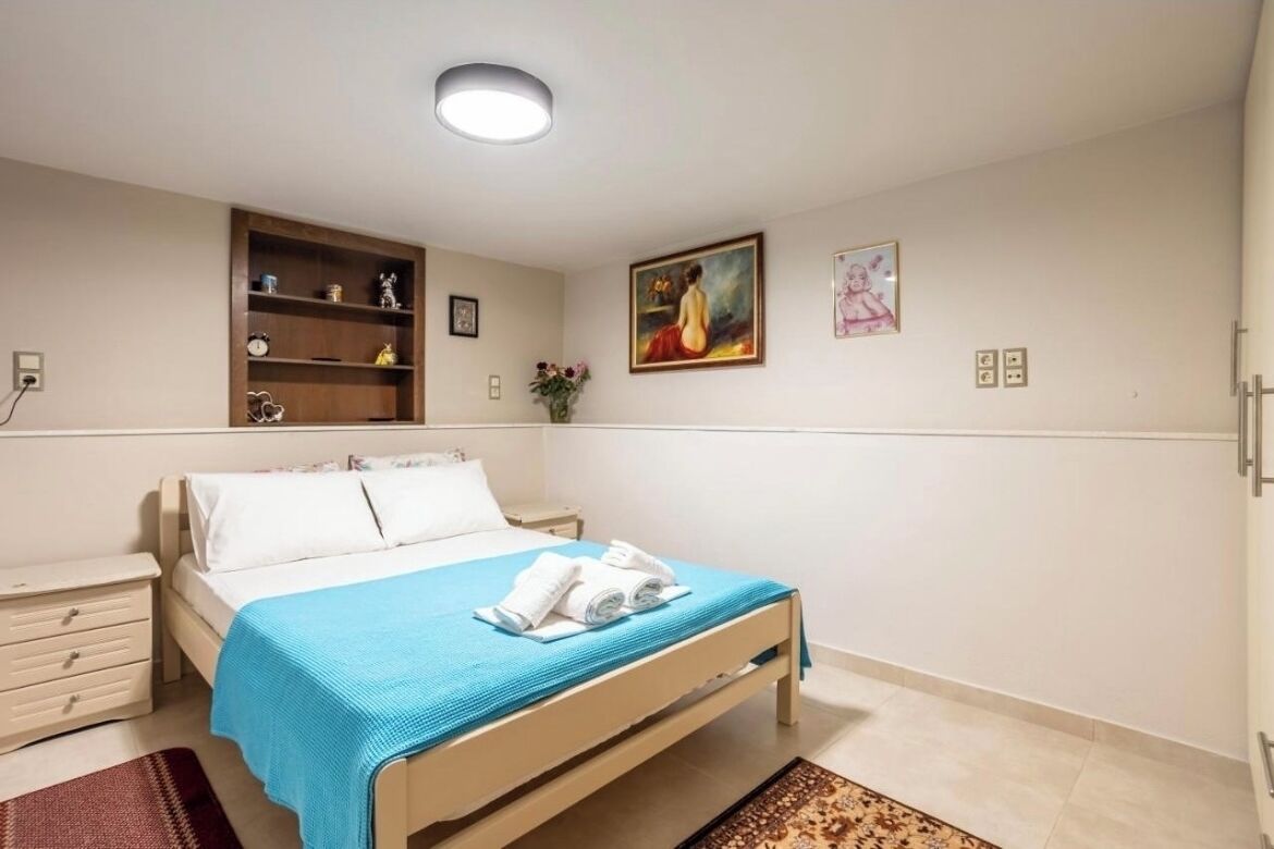 Une chambre à coucher comprenant un lit, une table de chevet, une commode, une étagère avec des objets décoratifs et un tableau au mur.
