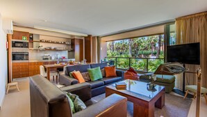 A modern living room with a sofa, coffee table, and TV. There's a kitchen area with cabinets and a dining table. - Algarve Golf & Golden Coast by Interhome (Gale)