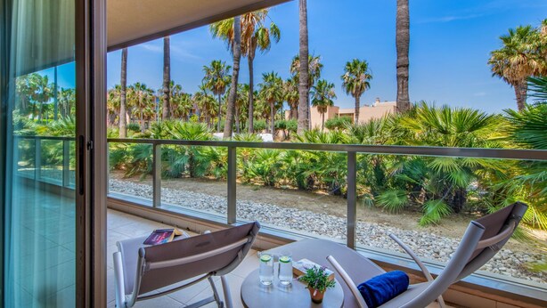 A balcony with two chairs, a table, and a view of palm trees and buildings. - Algarve Golf & Golden Coast by Interhome (Gale)