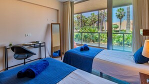 A hotel room with two beds, a desk, a chair, a large mirror, and a view of palm trees and a pool. - Algarve Golf & Golden Coast by Interhome (Gale)