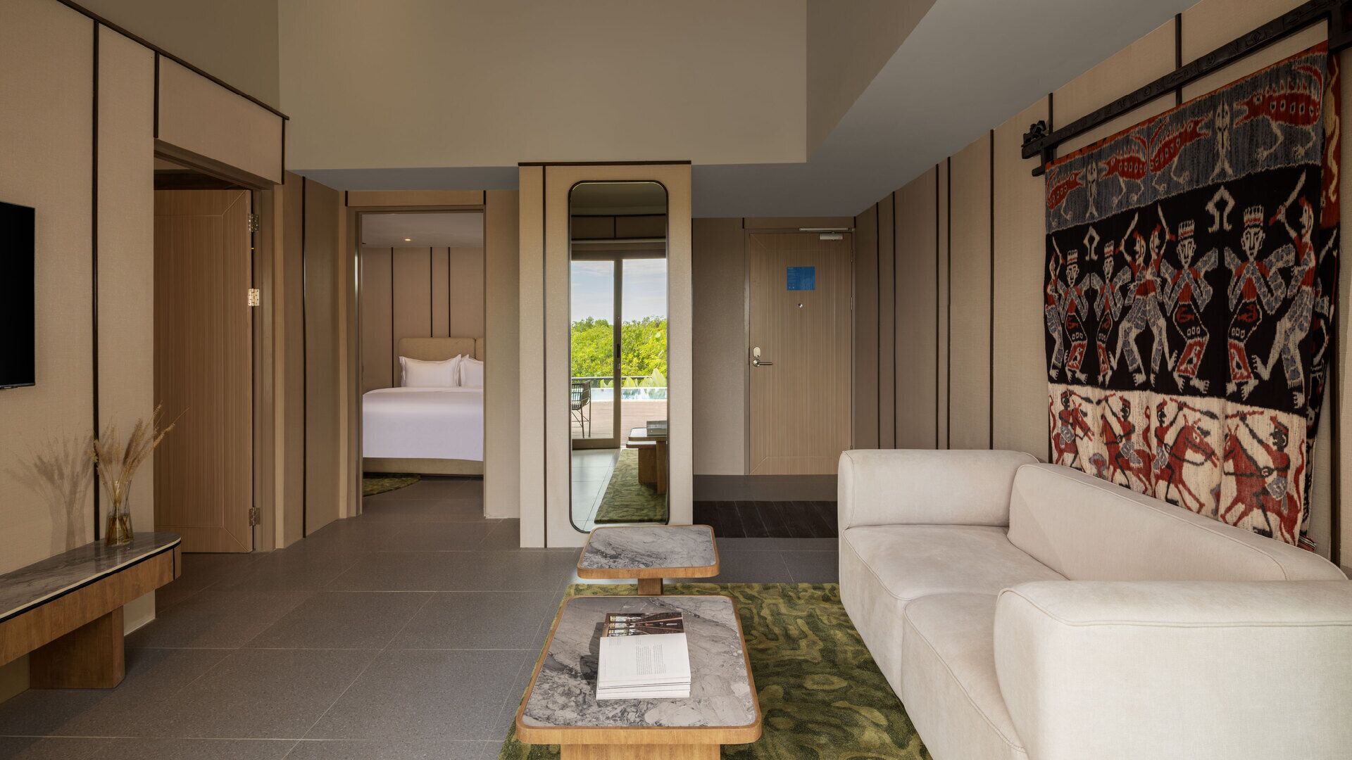 A modern hotel room with a bed, a sofa, a coffee table, and a large mirror.
