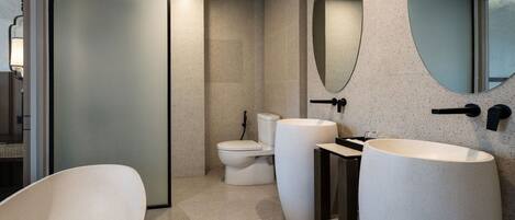 Un baño moderno con una bañera independiente, un inodoro y un lavabo con un espejo grande arriba.
