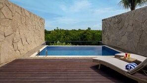 A pool area with stone walls, a wooden deck, and a lounge chair with a towel.