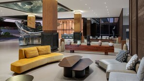 A modern lobby with a yellow sofa, a wooden bench, and a large sculpture.