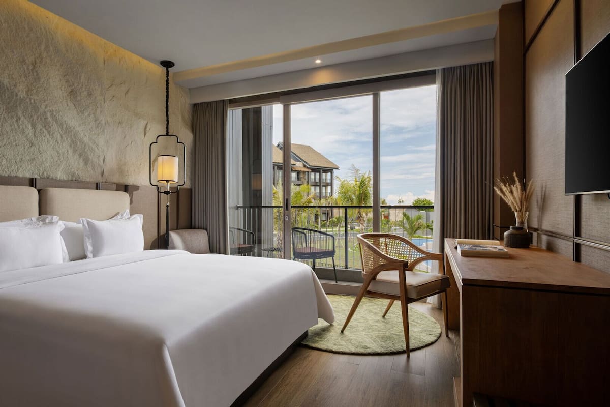 Habitación de hotel moderna con una cama grande, un escritorio, una silla y un balcón con vistas.