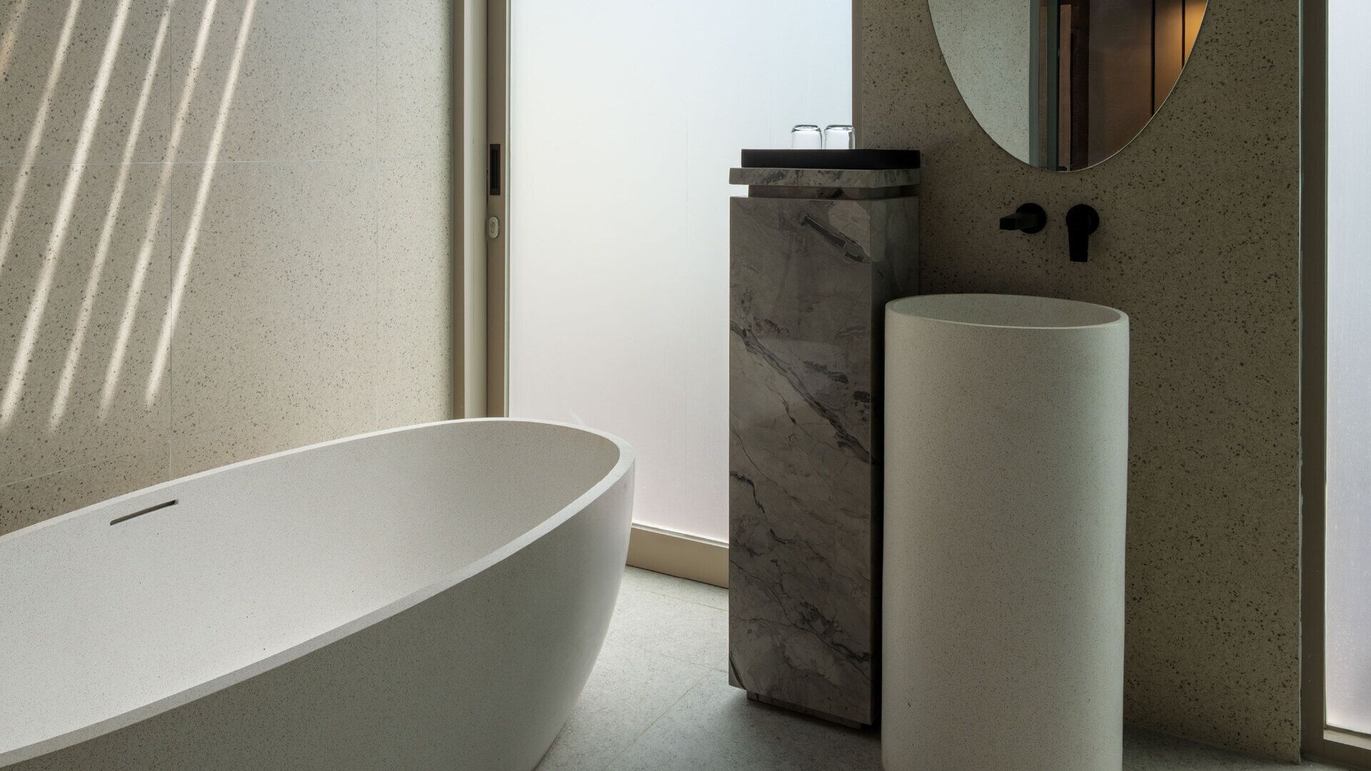 Un baño moderno con una bañera independiente, un cubo de basura de mármol y un lavabo cilíndrico.