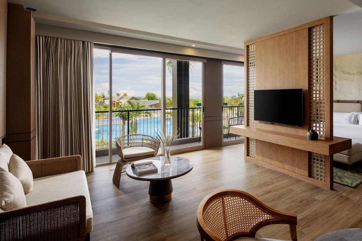 Habitación de hotel con balcón, televisión, cama y zona de comedor.