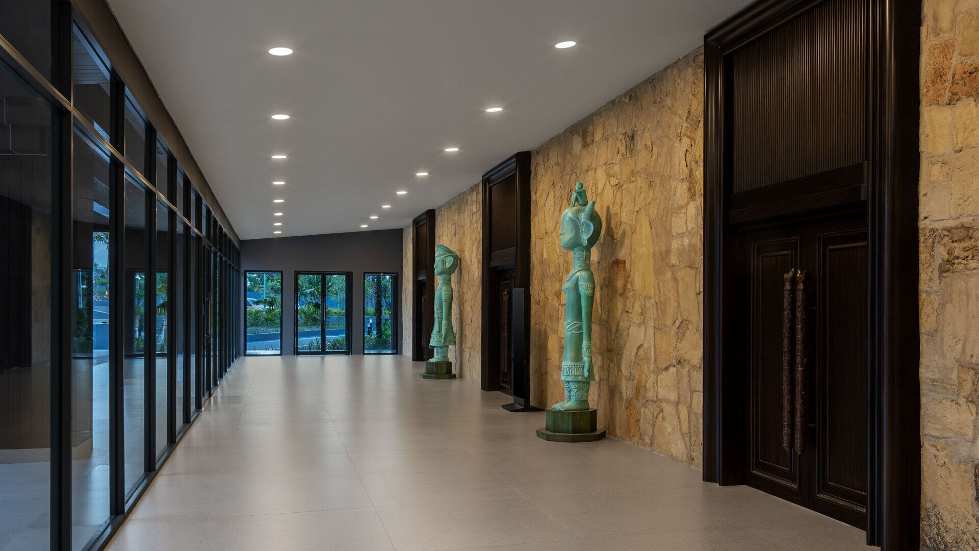 A modern hallway with glass doors, a stone wall, and three green statues.