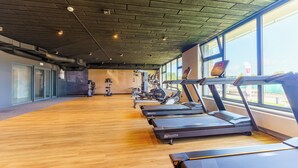 A gym with treadmills and exercise equipment, large windows, and a wooden floor.