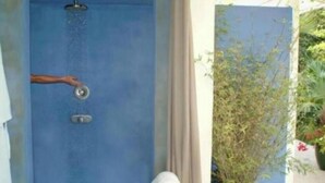 A blue shower enclosure with a hand turning a silver handle, a green stool with white towels, and a potted plant outside. - Private Hideaway w/ Balcony + Lush Views @Islamorada - Hideaway suite (Islamorada)