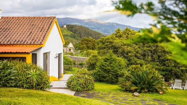 A white building with a red roof, surrounded by lush greenery and a mountainous backdrop. - Quinta do Ananás Pineapple Farm (Ponta Delgada)