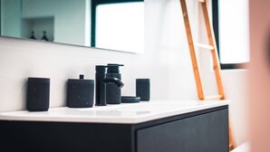 A modern bathroom with a white vanity, black fixtures, and a mirror reflecting a window and a ladder. - Quinta do Ananás Pineapple Farm (Ponta Delgada)