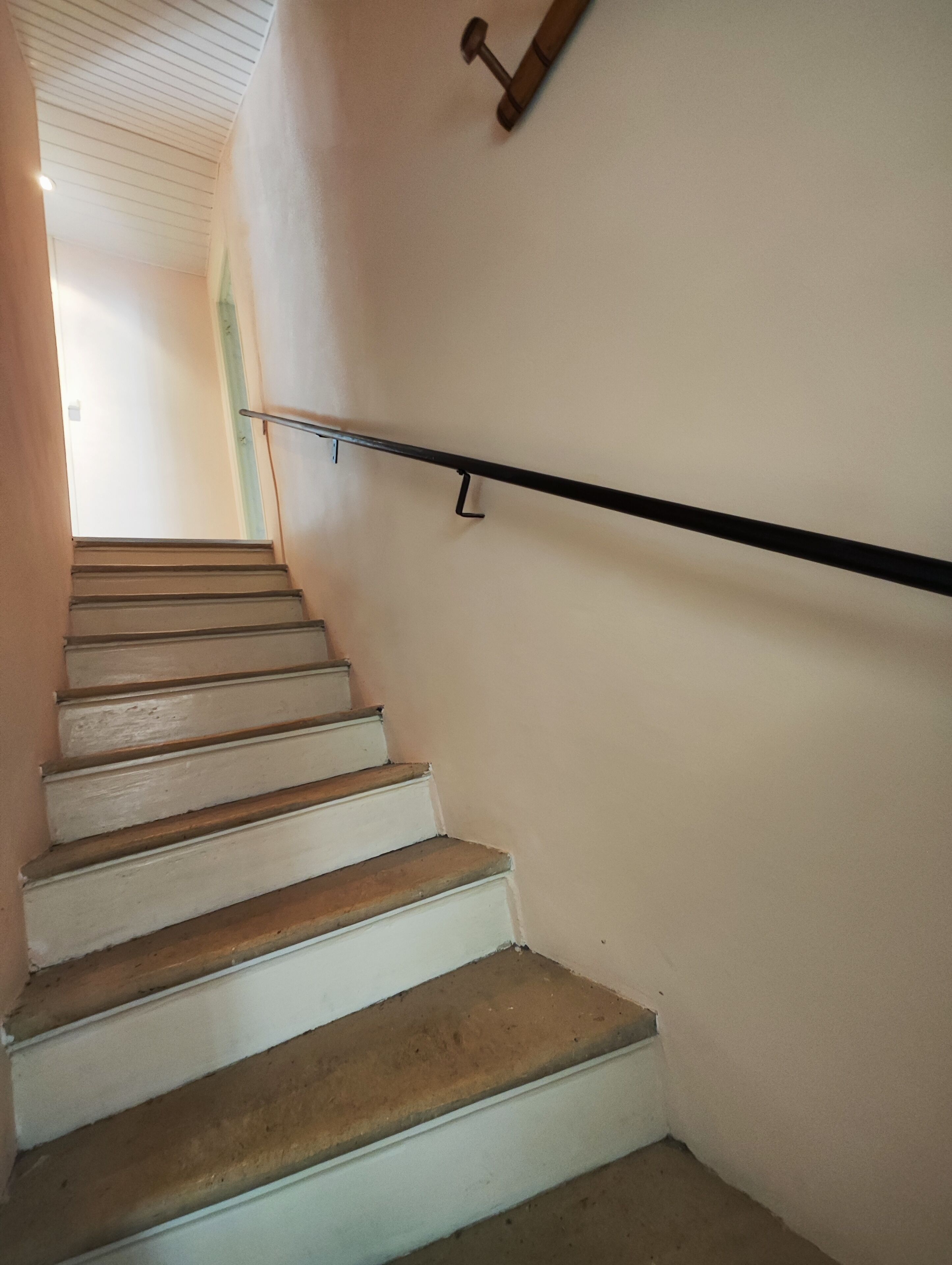 A staircase with white steps and a black handrail, leading to a room with a white ceiling and a green accent wall.