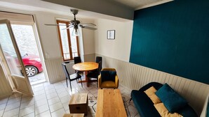 Uma sala de estar com mesa de centro de madeira, sofá com almofadas, mesa de jantar com cadeiras e ventilador de teto.
