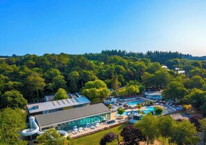 A resort with a swimming pool, lounge area, and a building with a glass facade. - Camping Le Ty Nadan (Locunolé)