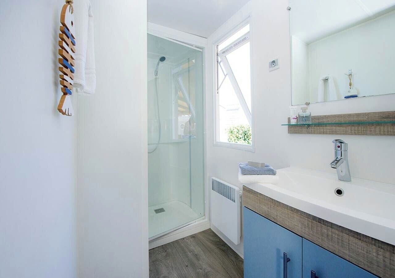 A modern bathroom with a glass shower enclosure, a white sink with a wooden countertop, and a blue cabinet.