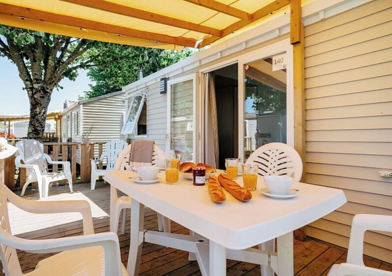 A covered outdoor dining area with a white table set for breakfast, including croissants and orange juice.