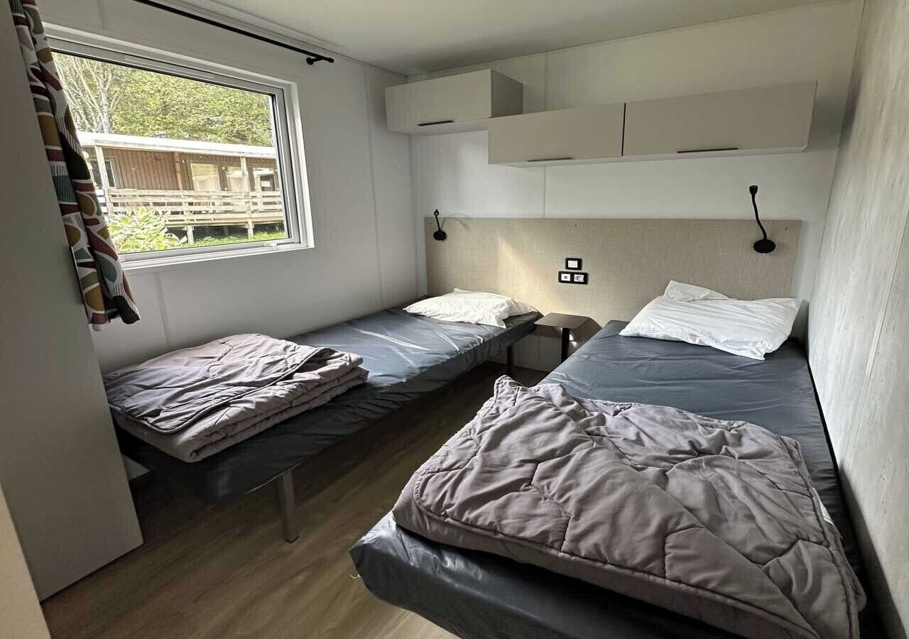 Een compacte kamer met twee eenpersoonsbedden, een raam met gordijnen en inbouwopbergkasten.