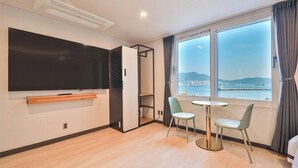 Una habitación de hotel moderna con un televisor grande, una mesa pequeña con dos sillas, un balcón con vistas al mar y un armario con puerta corredera.