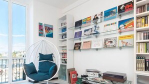 A modern living room with a hanging chair, a bookshelf filled with books and vinyl records, and a large window offering a view of the city. - Casa Dè Mà, Large Luxury House with View of the Old Port and Aquarium of Genoa (Genova)