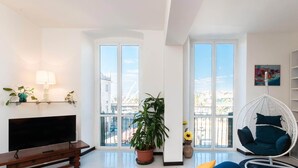 A modern living room with a flat-screen TV, a wooden bench, a hanging chair, and a bookshelf. - Casa Dè Mà, Large Luxury House with View of the Old Port and Aquarium of Genoa (Genova)