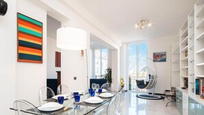 A modern dining area with a glass table, clear chairs, and a hanging chair. - Casa Dè Mà, Large Luxury House with View of the Old Port and Aquarium of Genoa (Genova)