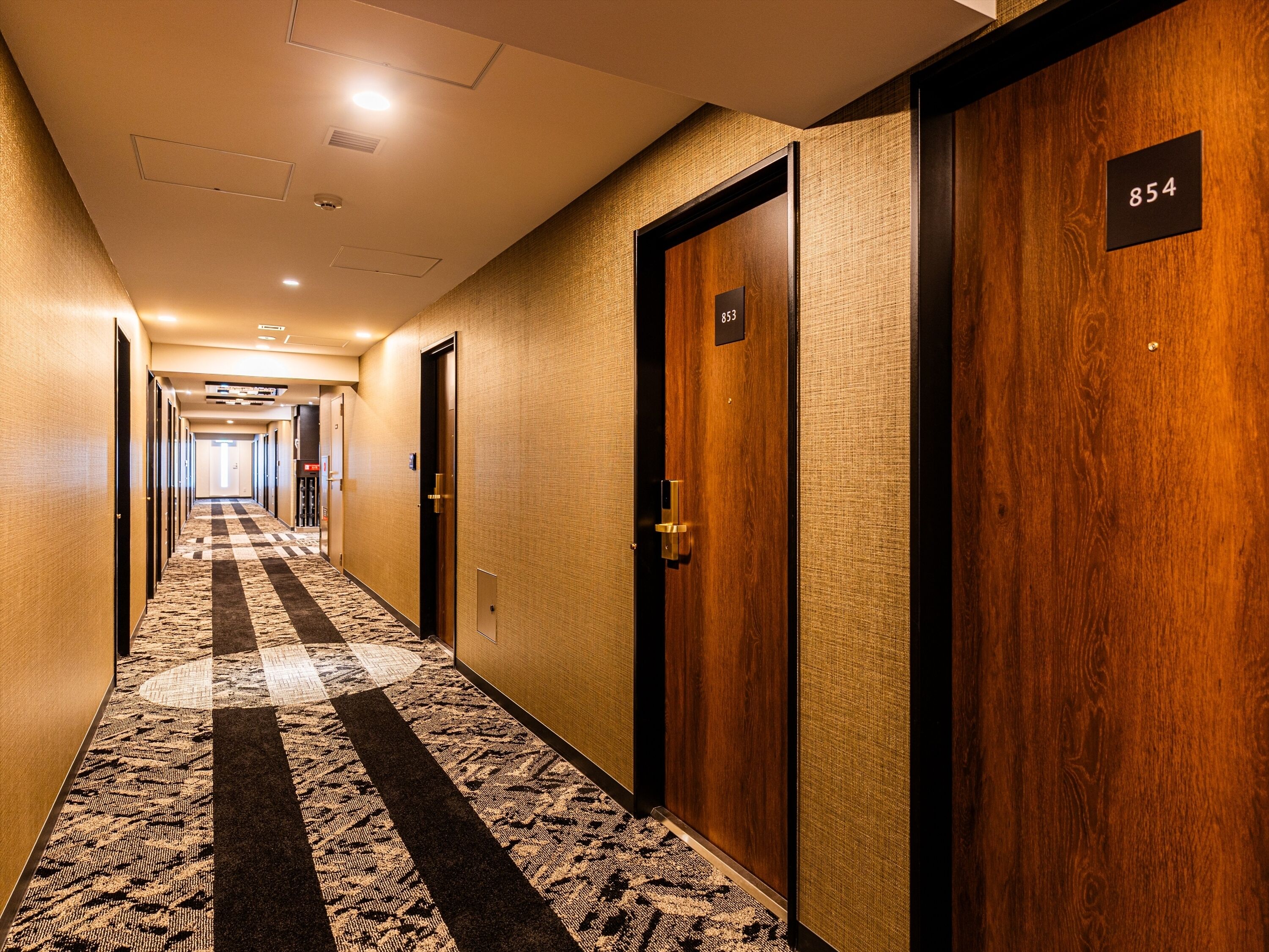 Un pasillo de hotel con pisos alfombrados, puertas de madera y letreros con números de habitación.