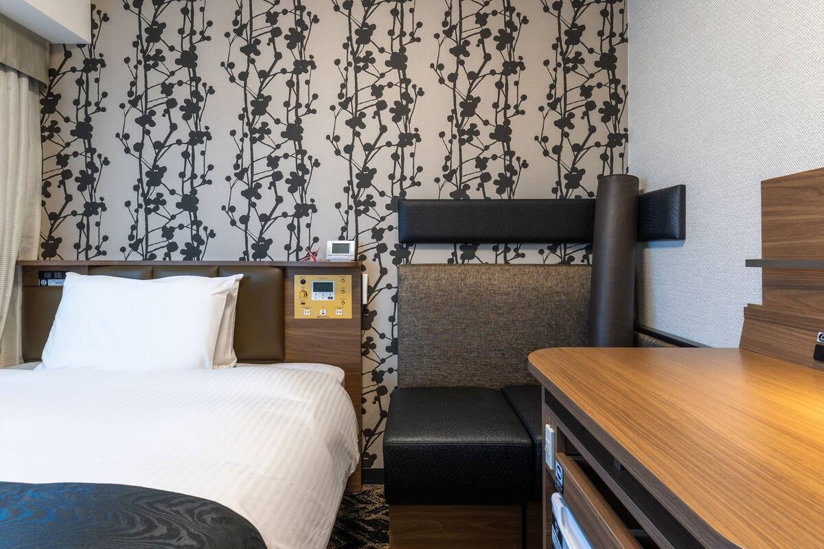 Ein Hotelzimmer mit Bett, Schreibtisch, Stuhl, Bedienfeld und Wand mit Blumenmuster.